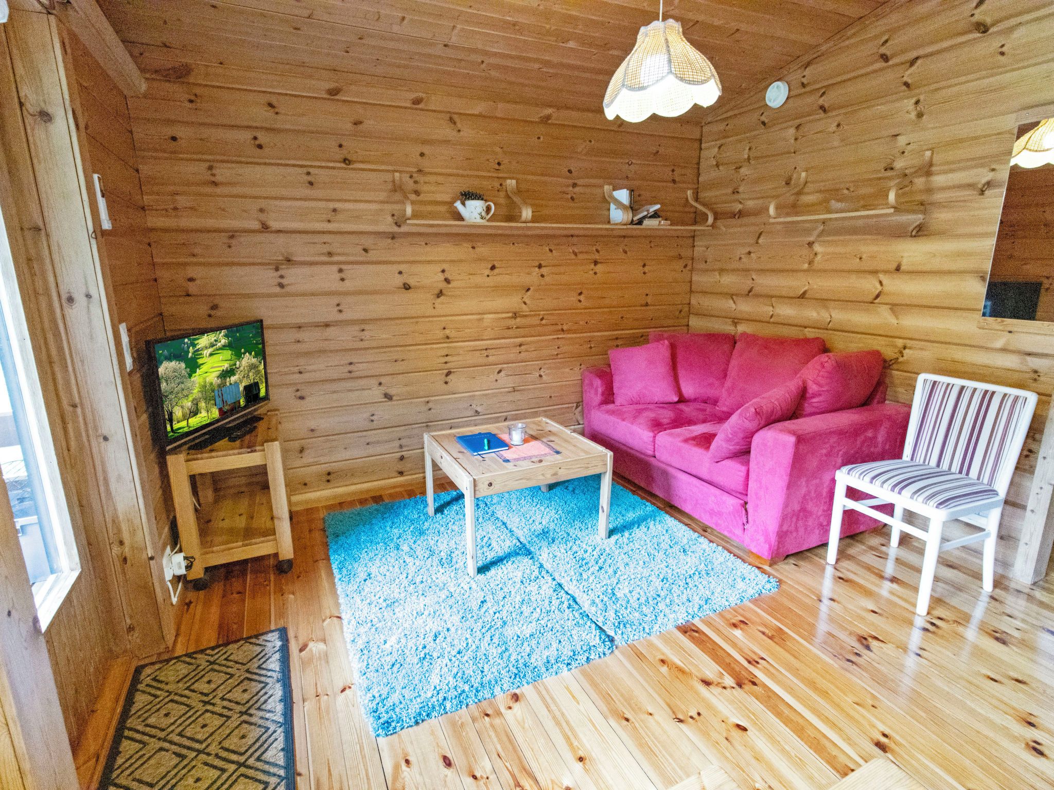L’intérieur d’un chalet accueillant, avec un plancher en bois, un canapé rose, une chaise blanche, une table basse et un téléviseur posé sur un meuble en bois.