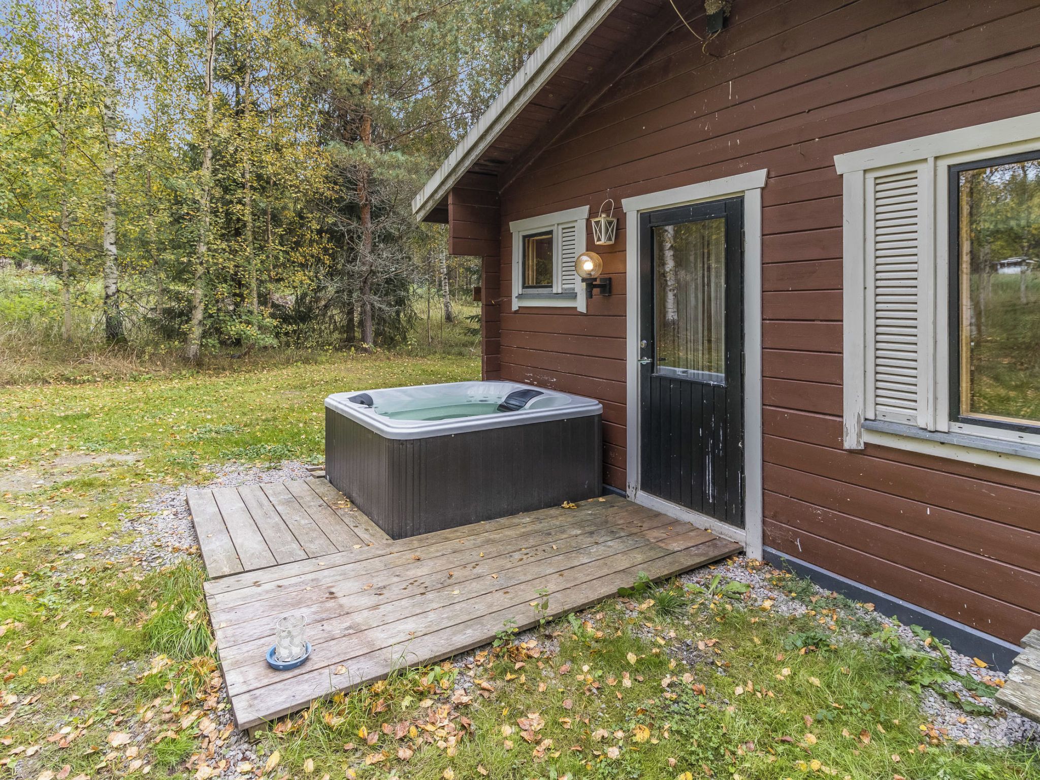 En stuga av trä med ett bubbelbad, en veranda och en dörr med ett fönster.