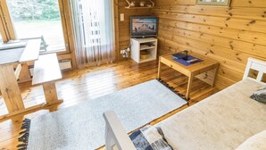 Un interior de cabaña acogedor, con paredes de madera, un televisor sobre un mueble bajo y una zona de comedor con bancos.