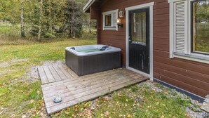 Una cabaña de madera con un jacuzzi en una terraza de madera, rodeada de árboles.