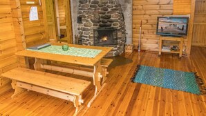 Ein gemütliches Blockhaus-Interieur mit Kamin aus Stein, Holzmöbeln und einem Fernseher.