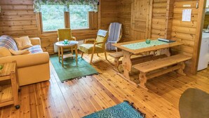 Ein gemütliches Blockhaus-Interieur mit Holzboden, einer Couch, zwei Sesseln, einem Esstisch und einer Bank.