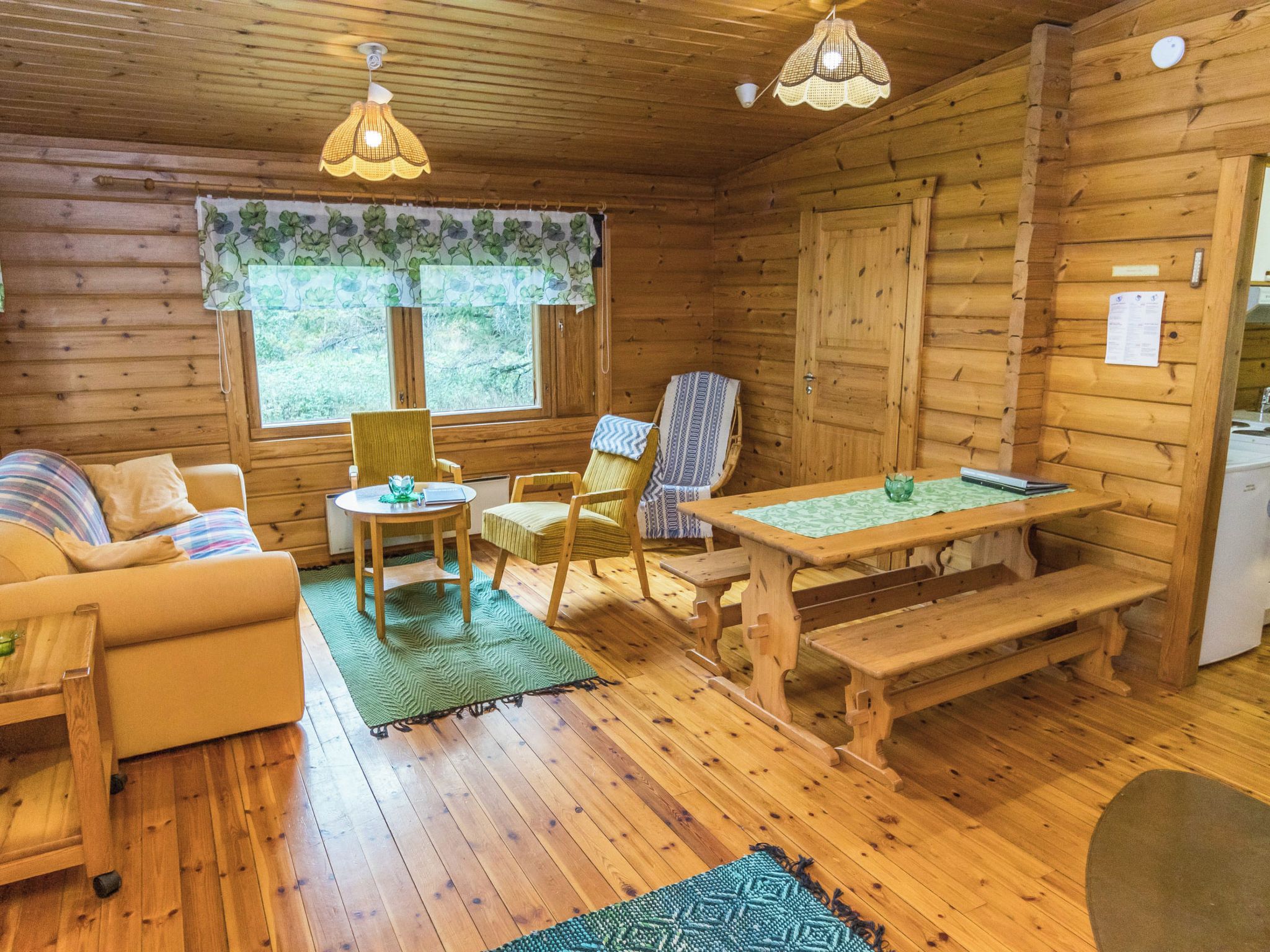 Un accogliente interno di una baita con pavimento in legno, un divano, un tavolo da pranzo con sedie e una panca.