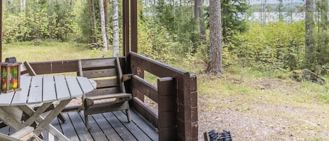 Een houten terras met een tafel en banken, omringd door bomen en uitzicht op een meer.