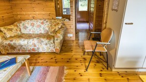 L’intérieur d’un chalet chaleureux, avec un canapé à motifs floraux, un plancher en bois et une porte donnant sur l’extérieur.