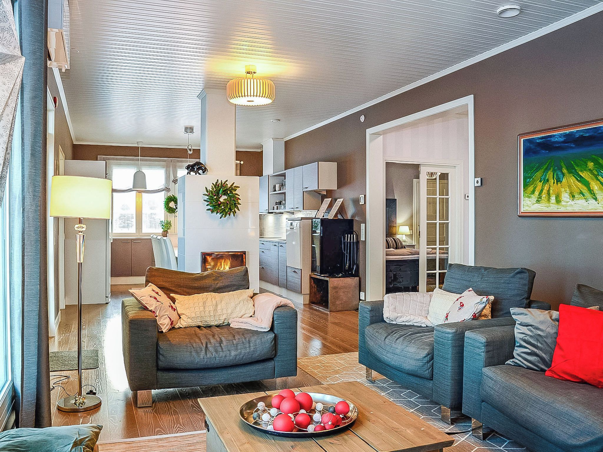 Un salon moderne avec deux canapés, une table basse ornée d’objets décoratifs rouges, une cheminée et, au fond, une cuisine.