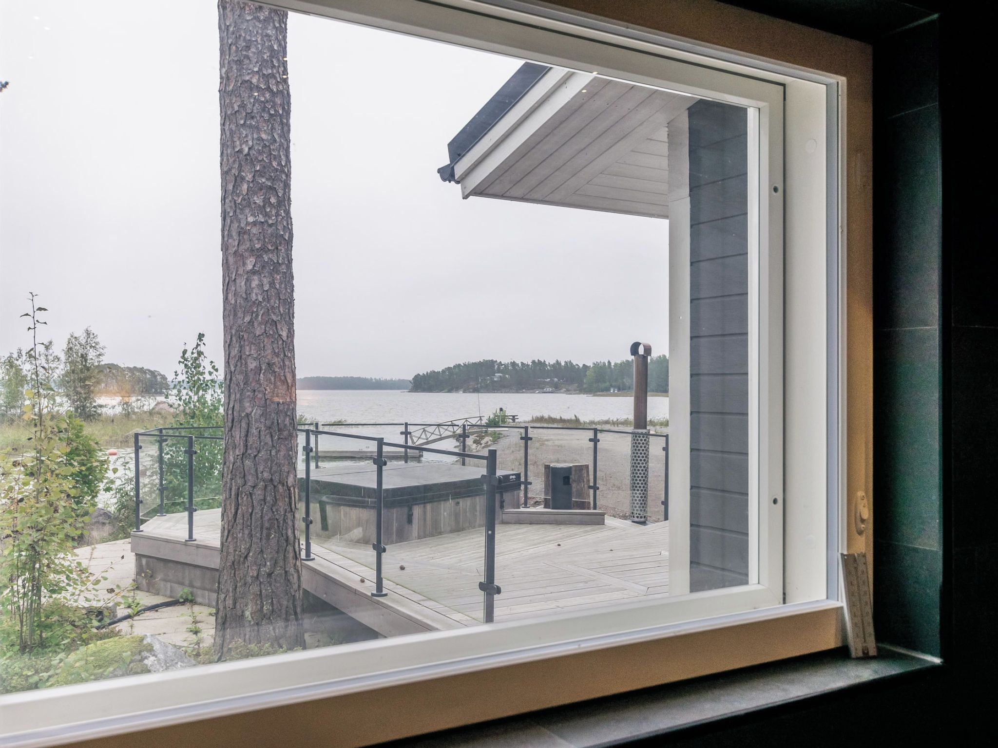 Une vue depuis une fenêtre donnant sur une terrasse avec une balustrade, un arbre et une côte lointaine.