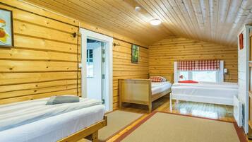 Una cabaña con paredes y pisos de madera, dos camas individuales, una mesita y una ventana con cortina a cuadros.
