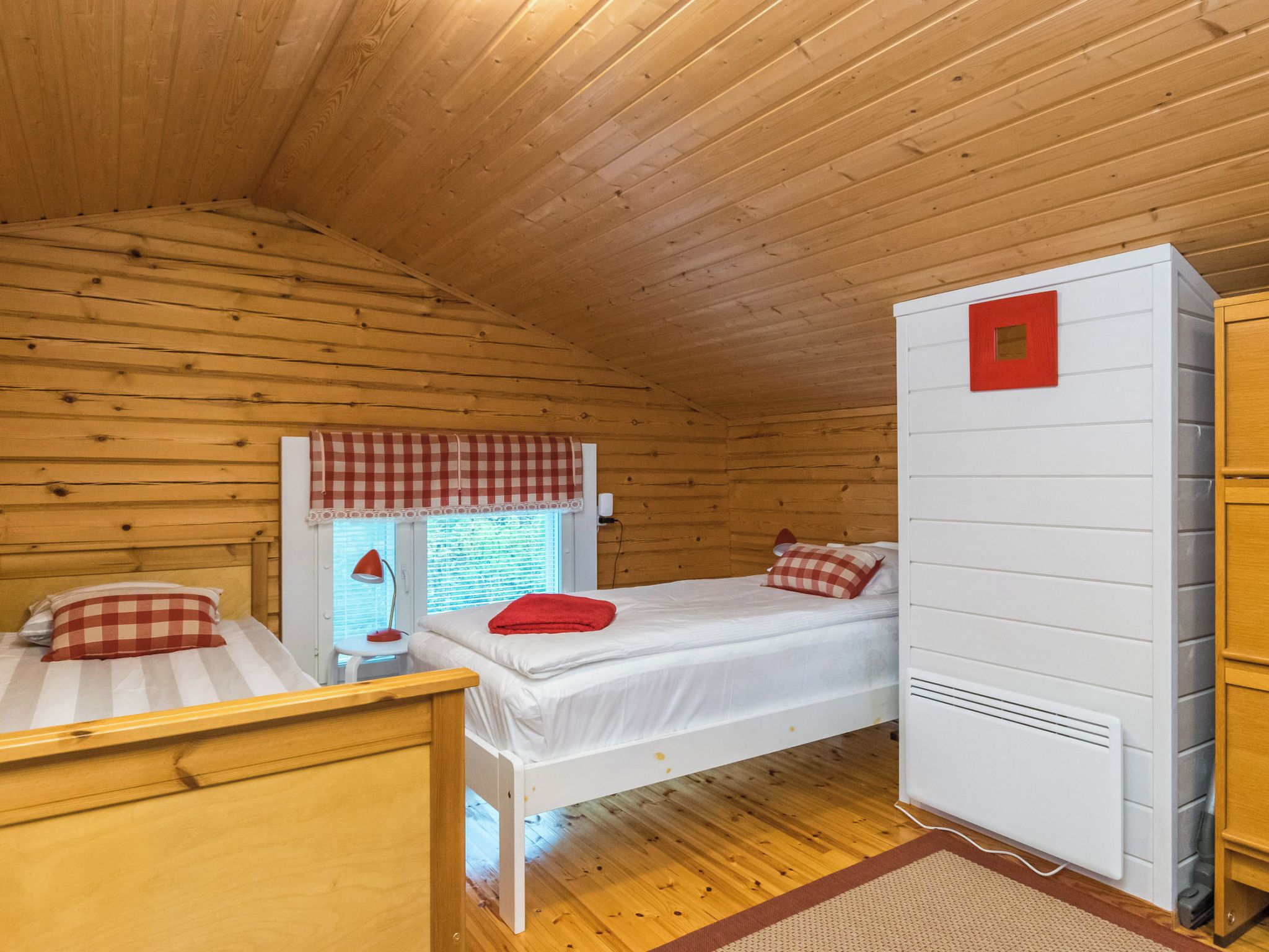 A cabin with two wooden beds, a window with blinds, a red lamp, and a white wardrobe.