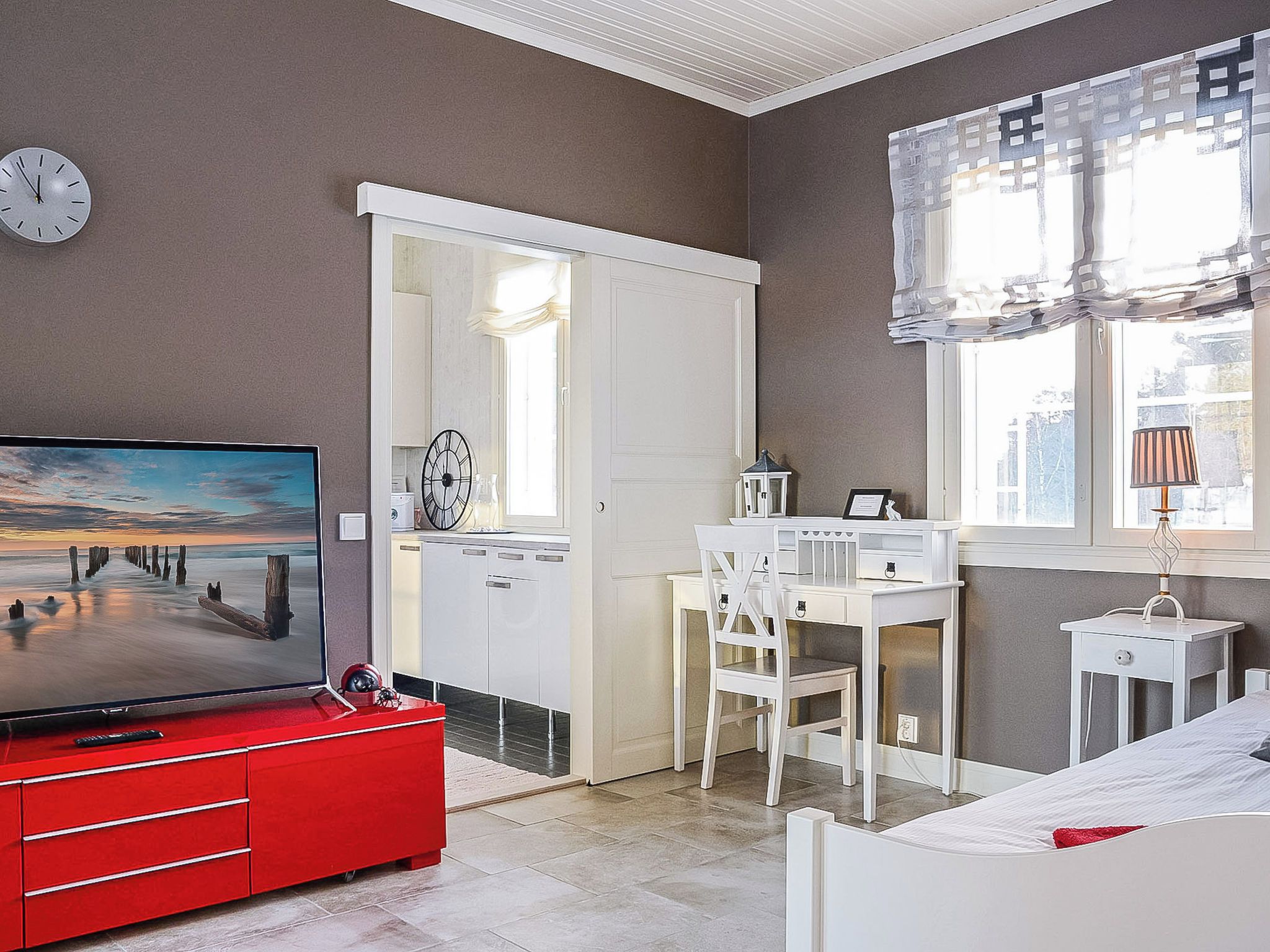 Een slaapkamer met een televisie, bureau, stoel, bed en een raam met gordijnen.