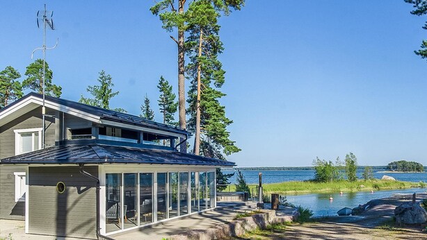 A two-story house with a large glass conservatory, a dock extending into a lake, and a clear view of the surrounding forest and water. - Villa nyåker by Interhome (Porvoo)