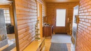 L'intérieur d'une cabane en rondins, avec un banc en bois, une petite table surmontée d'un vase, un mur en briques et une porte en bois.