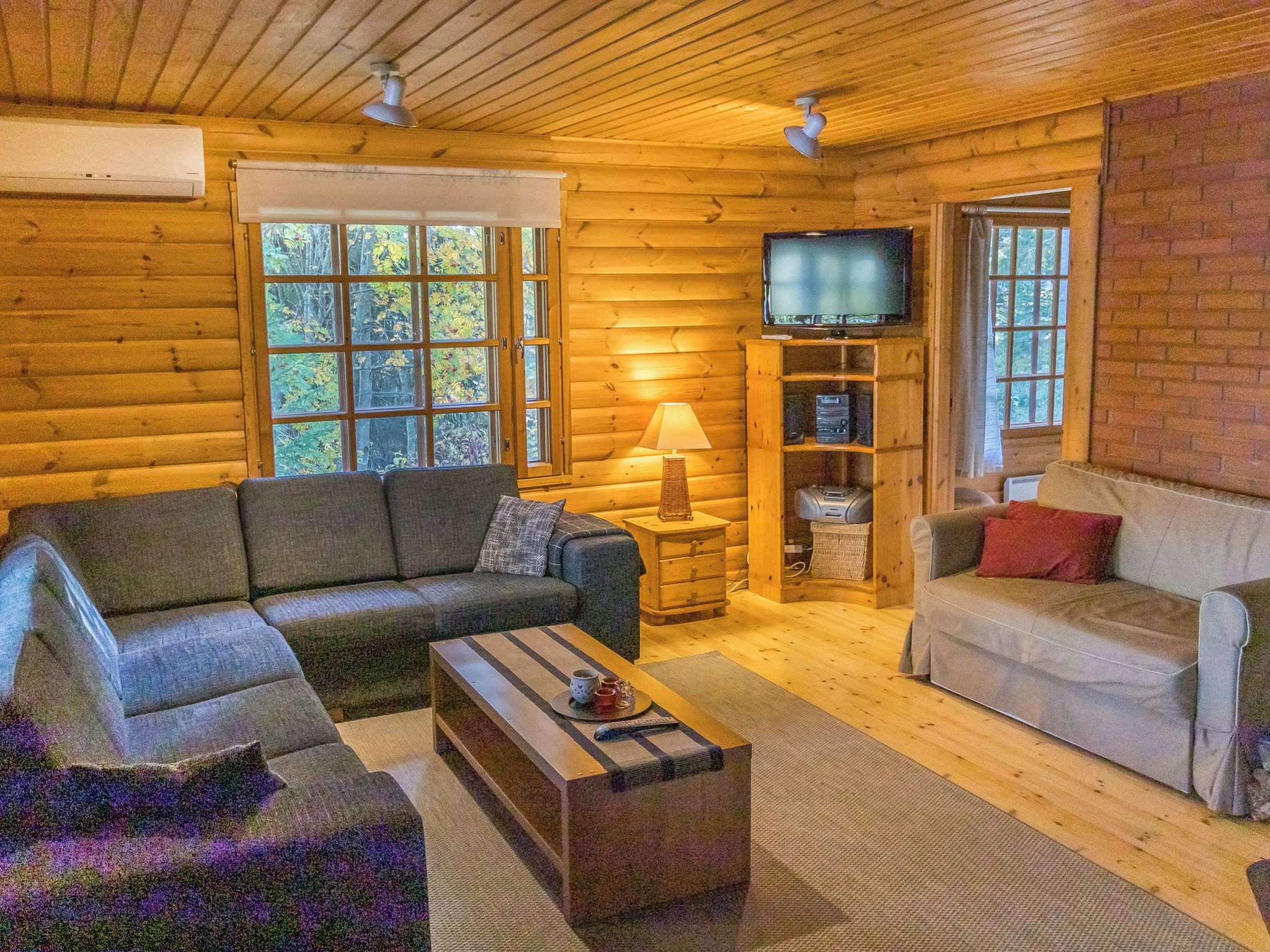 L’intérieur d’une cabane en rondins, avec un canapé, une table basse, un téléviseur et une lampe.