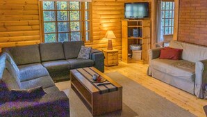 L’intérieur chaleureux d’un chalet, avec un revêtement mural en bois, un canapé, une table basse, un téléviseur et une bibliothèque.