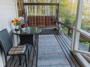 A wooden deck with a glass table and chairs, a woven rug, and a view of trees. - Vacation home Laura by Interhome (Outokumpu)