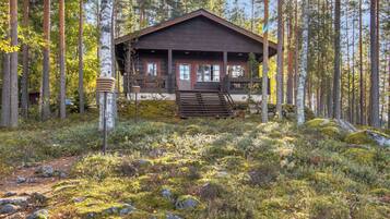Eine Holzhütte, umgeben von einem Wald mit hohen Bäumen und einem mit Moos und Steinen bedeckten Boden.