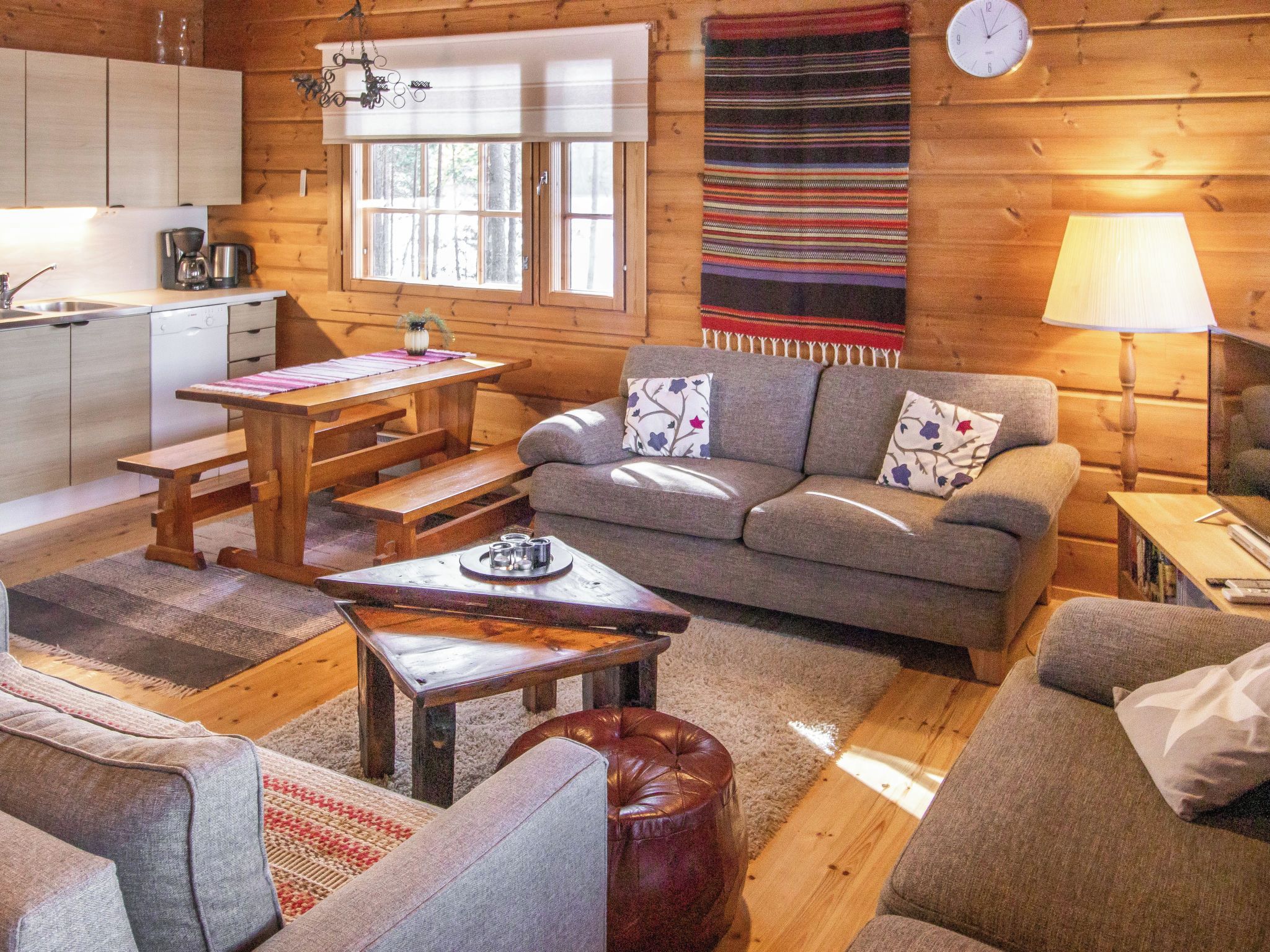 Ein gemütliches Blockhaus-Interieur mit einem Holzesstisch, einer Couch und einer Küchenzeile mit Kaffeemaschine.