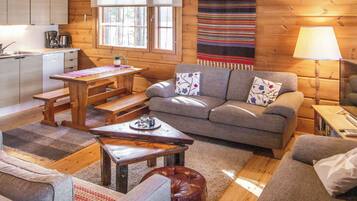 Ein gemütliches Blockhaus-Interieur mit einem Holzesstisch, einer Couch und einer Küchenzeile mit Kaffeemaschine.