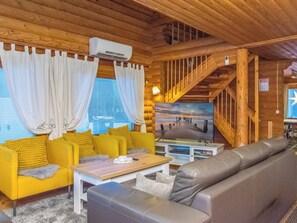 A cozy cabin interior with a wooden staircase, a sofa set, a television, and a dining area.