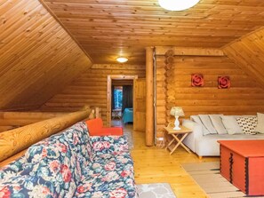 A log cabin interior with a sofa, a small table with a lamp, and a red ottoman.