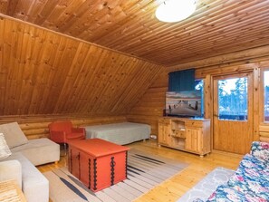 L’intérieur d’un chalet confortable, avec un canapé, une commode rouge, un téléviseur posé sur un meuble en bois et une fenêtre donnant sur la forêt.