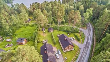 Un quartier résidentiel composé de plusieurs maisons, entouré d’une forêt dense, avec un lac en arrière-plan et une route sinueuse.