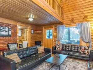 A log cabin interior with a black leather sofa set, a small coffee table, and a brick wall with a framed picture.