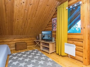 A cozy cabin room with a wooden interior, a television on a wooden stand, a window with curtains, and a star-patterned rug.