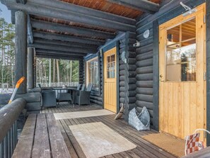 Une cabane en rondins dotée d’une terrasse en bois, d’un espace extérieur couvert avec des sièges et d’une porte donnant sur l’intérieur.