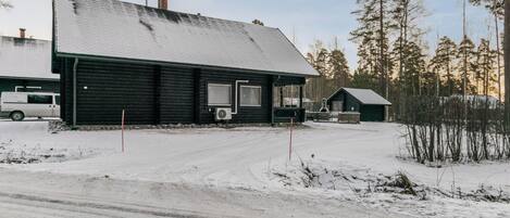 A snow-covered landscape with a black building featuring a large window and an air conditioning unit.