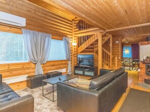 L’intérieur d’une cabane en rondins, avec une cheminée, un escalier et un coin salon comprenant des canapés et une table basse.