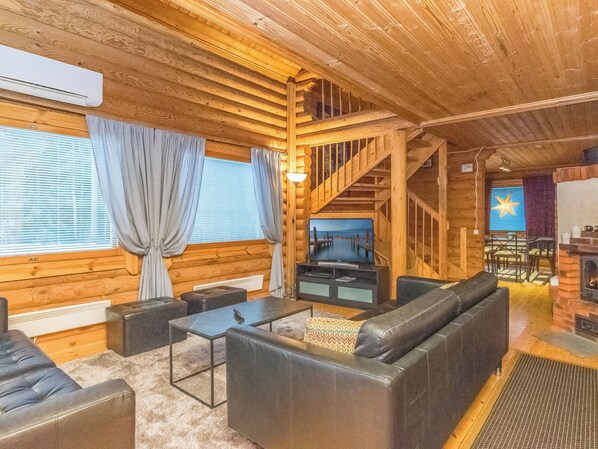 A log cabin interior with a fireplace, a staircase, and a seating area with sofas and a coffee table.