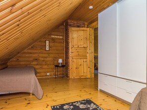 A bedroom with a sloped ceiling, wooden walls, a bed, a nightstand with a lamp, and a wardrobe.