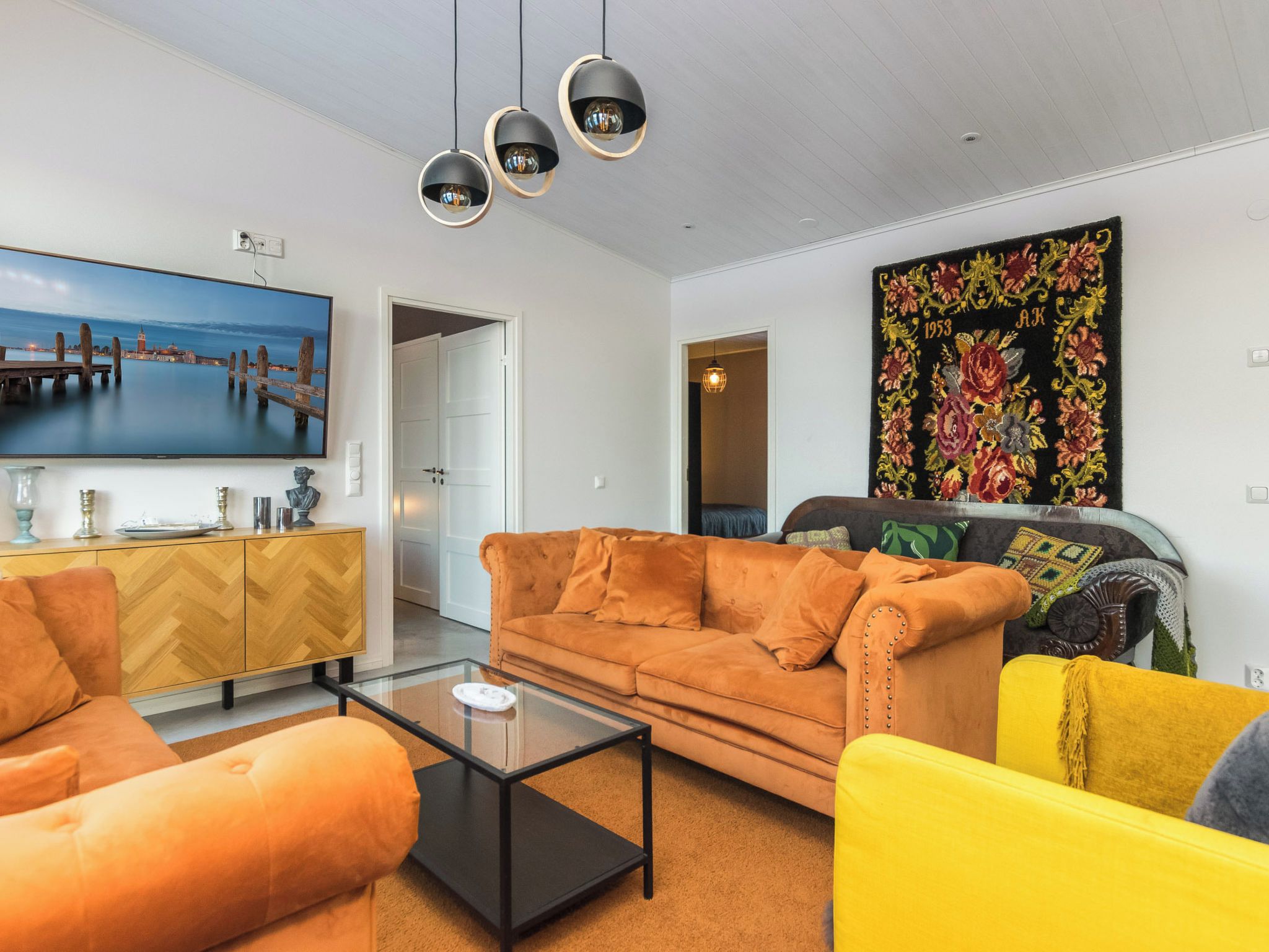 Una sala de estar con un sofá, sillones, una mesa de centro, un televisor y un cuadro.