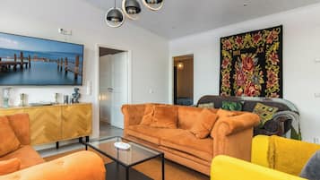 Una sala de estar con un sofá, sillones, una mesa de centro, un televisor y un cuadro.