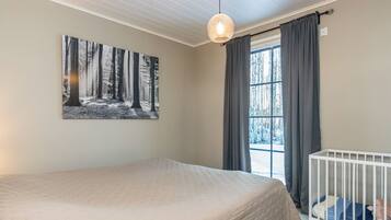 A bedroom with a bed, a crib, a window with curtains, and a wall-mounted light fixture.