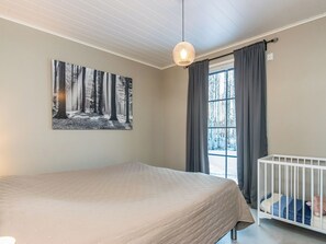 Une chambre à coucher avec un lit, un berceau, une fenêtre avec des rideaux et un luminaire fixé au mur.