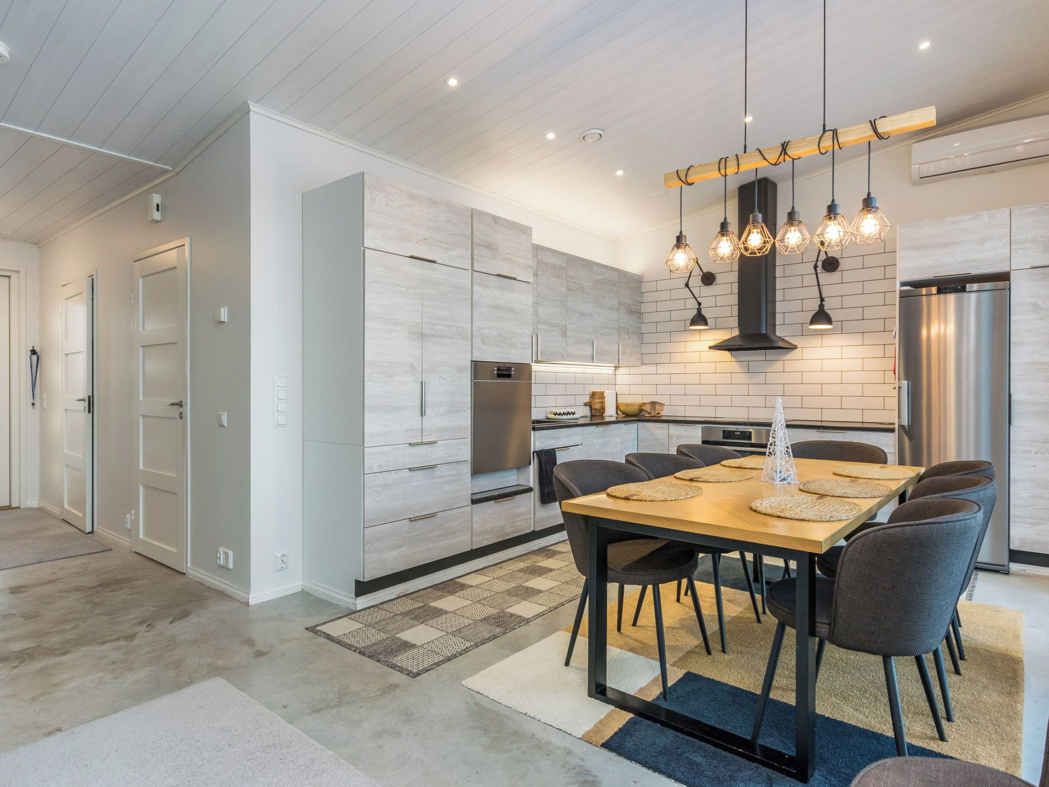 Una cocina moderna con zona de comedor, que incluye una mesa de madera, sillas e iluminación colgante.