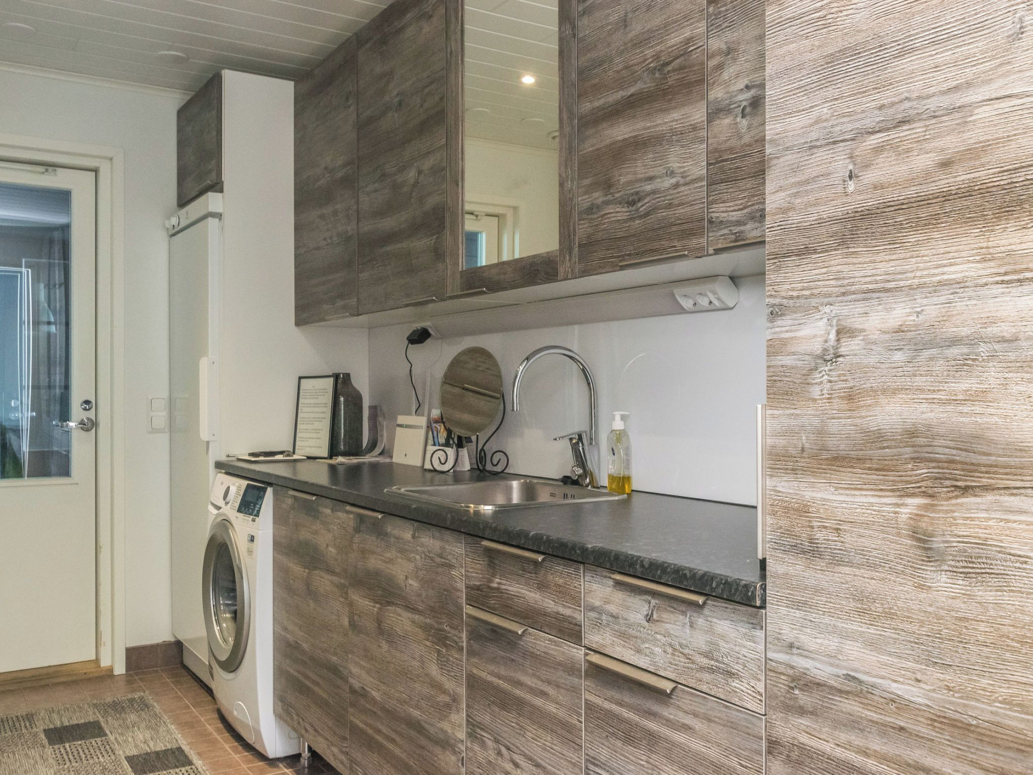A compact kitchen with a washing machine, a sink, and wooden cabinets.