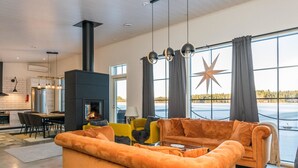A modern living room with a large orange sofa, a fireplace, and a view of a lake through large windows.