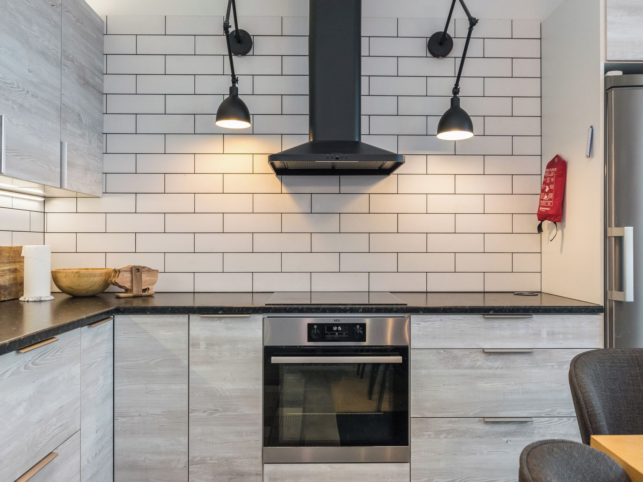 A modern kitchen with a built-in oven, a stove, and two pendant lights.