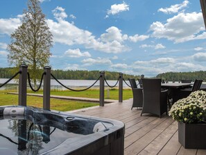 A hot tub on a wooden deck with outdoor furniture and a view of a lake.