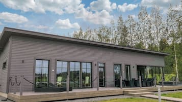 A modern building with large windows, a covered outdoor seating area, and a grassy lawn.