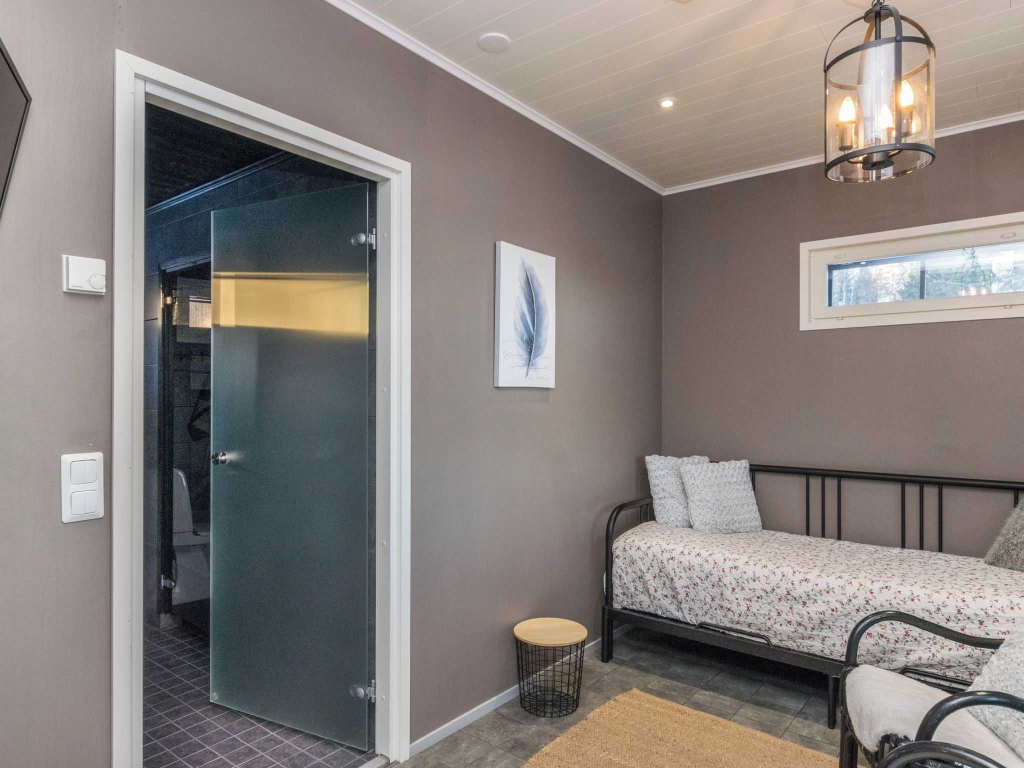 A bedroom with a bed, a bedside table, a chair, a small rug, a picture on the wall, a window, and a door leading to another room.