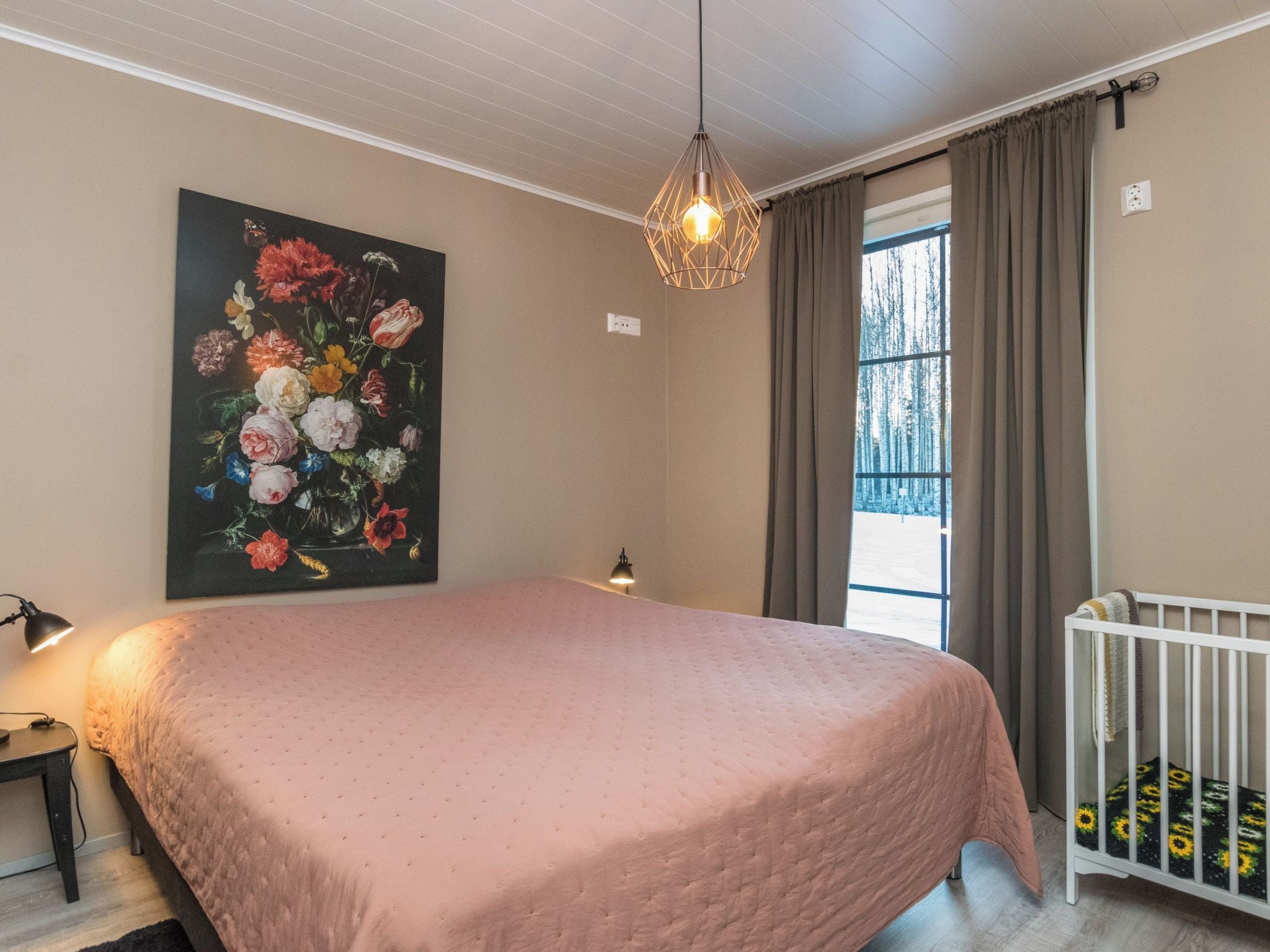 Un dormitorio con una cama grande, un cuadro de flores, una ventana con cortinas y una lámpara colgante.