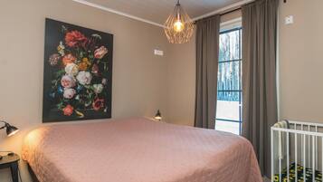 Ein Schlafzimmer mit einem großen Bett, einem Blumenbild, einem Fenster mit Vorhängen und einer Hängeleuchte.