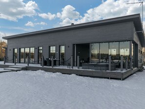 En moderne bygning med fladt tag, store vinduer og et overdækket udendørsareal.
