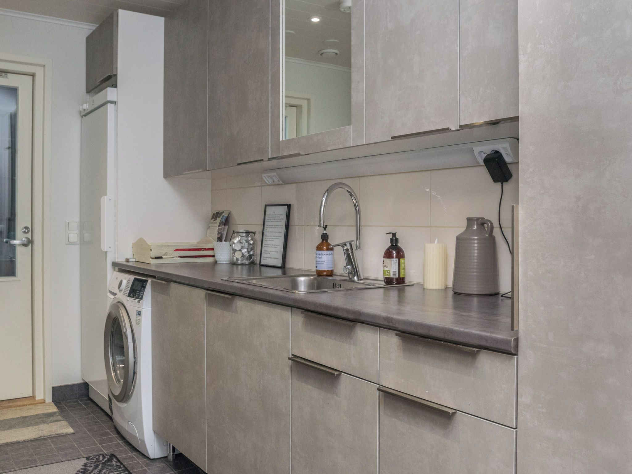 A modern kitchen with a built-in washing machine, stainless steel sink, and a large mirror above the countertop.