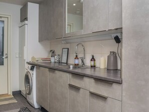 A modern kitchen with a built-in washing machine, stainless steel sink, and a large mirror above the countertop.