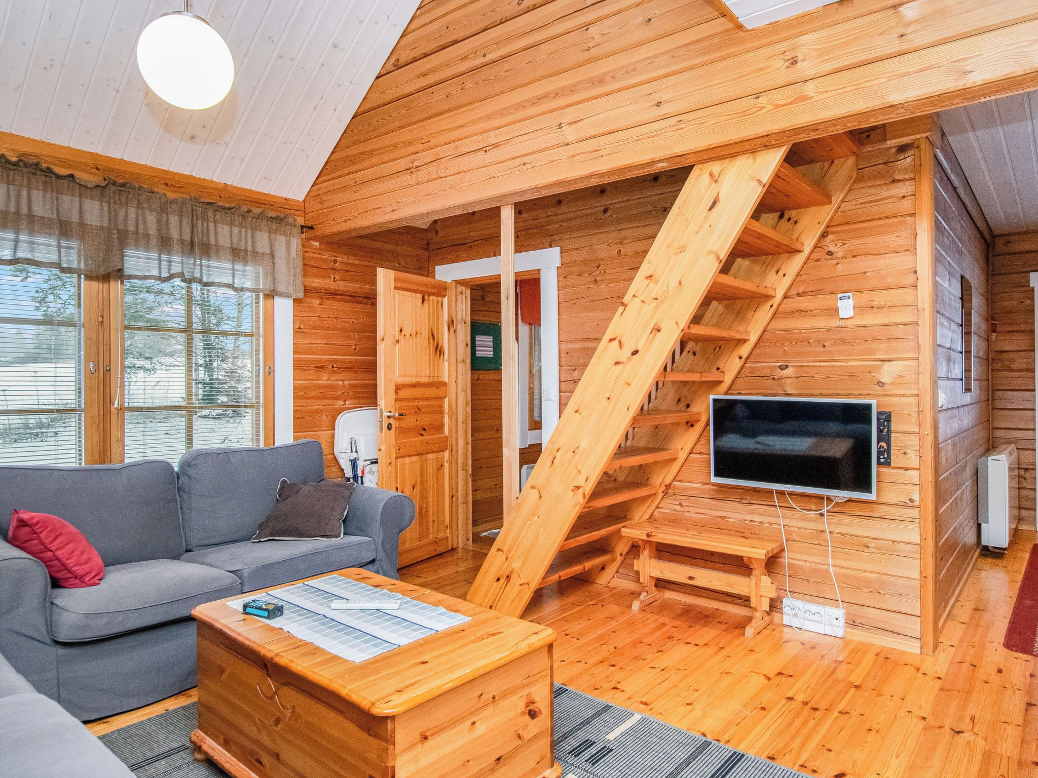 Interior acogedor de una cabaña con un sofá, una mesa de centro de madera, un televisor y una escalera.